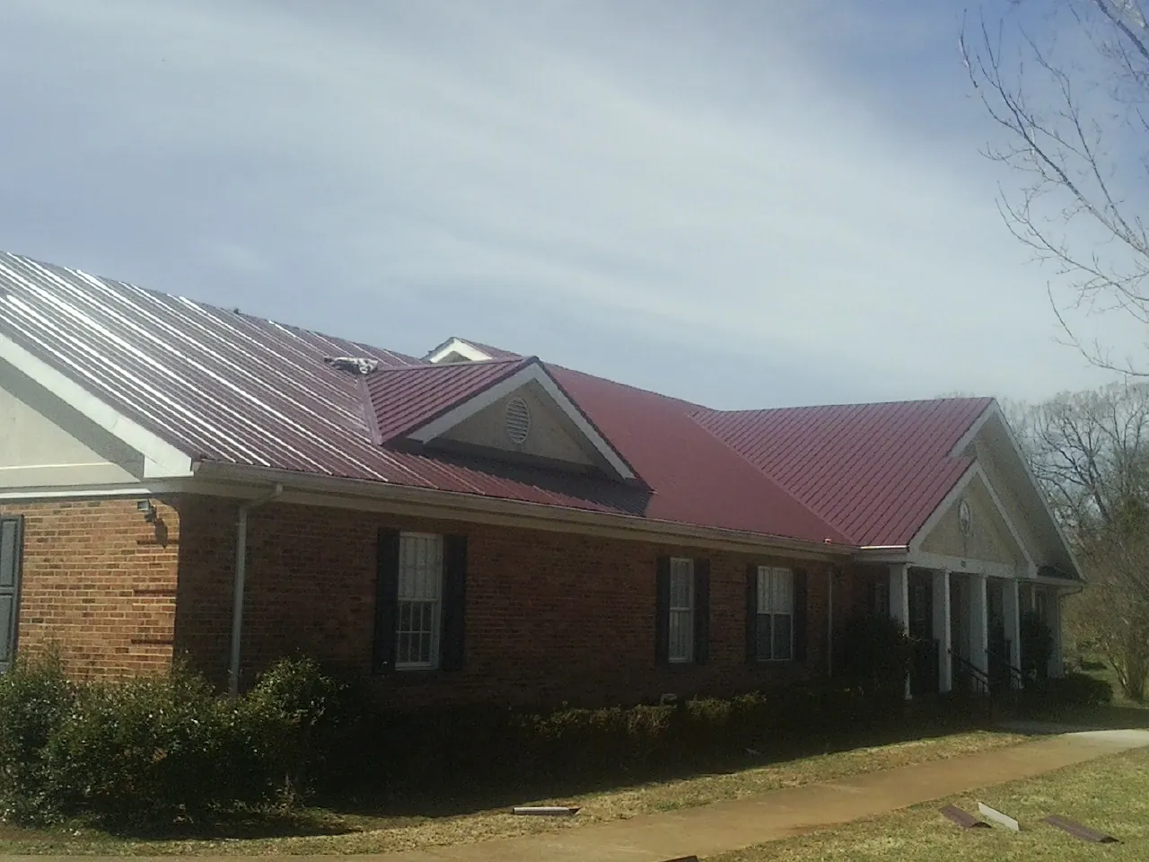 Red metal roof with gabled entries on a long brick building, from a Hail Damage Roof Repair job in Carbon Hill