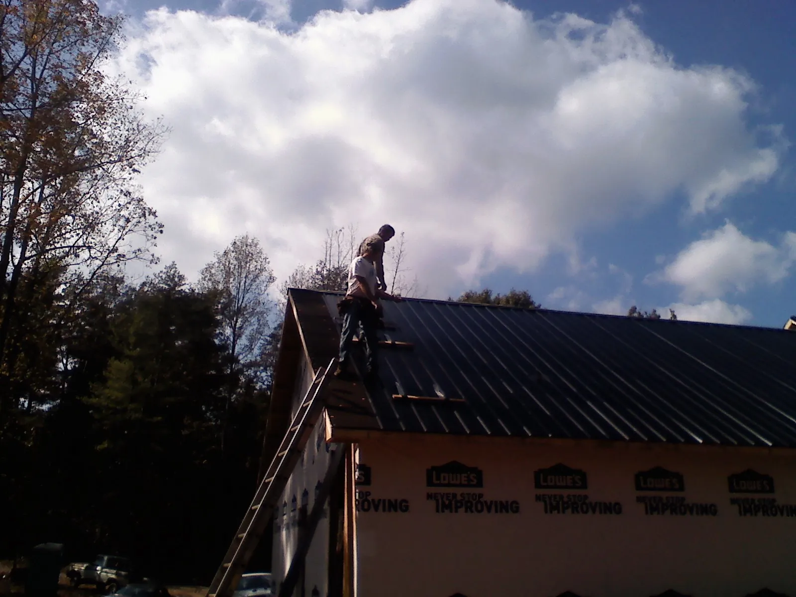 Roofer fastening dark metal panels high against a cloudy sky, from a Roof Inspection job in Carbon Hill