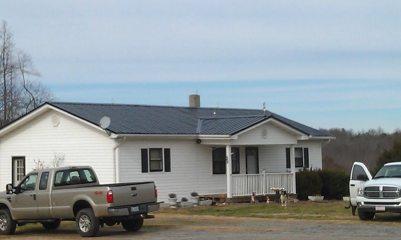Finished dark metal roof on a white ranch home with work trucks parked in Carbon Hill
