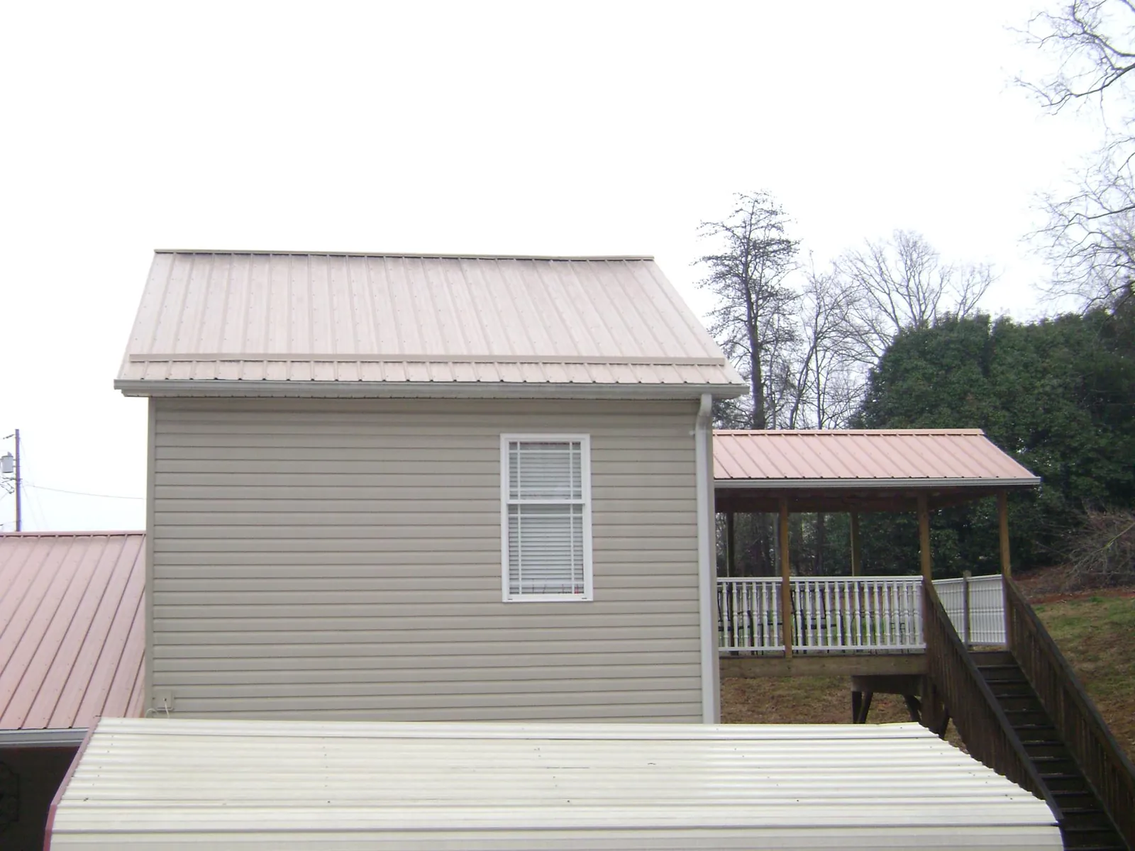 Tan metal roofs on a two story addition and attached porch, from a Roof Replacement job in Carbon Hill